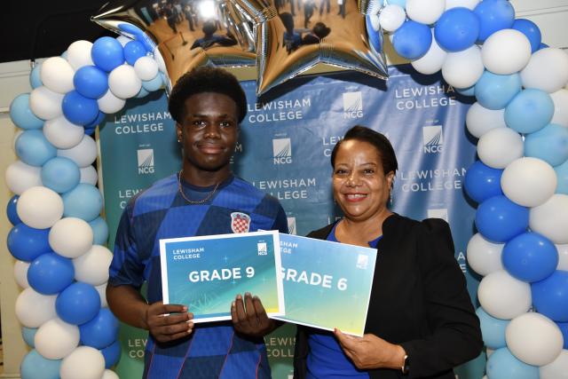 mayor of lewisham, Brenda Dacres stands with a student. They are standing in front of a lewisham college media wall and both holding a card that says grade 9 and grade 6
